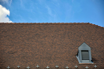 Fragment of the old tiled roof against the blue sky with clouds, architectural details of an old building.