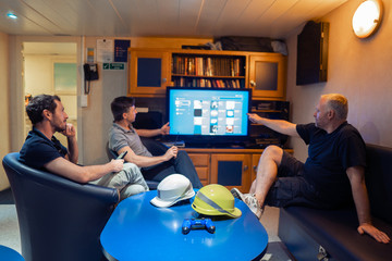 Happy team of ship officers watch TV onboard of vessel. TV, recreation and internet at sea