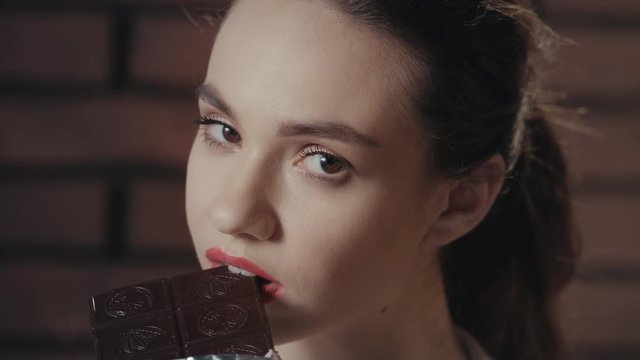Attractive woman biting and eating black chocolate. Face girl eating chocolate