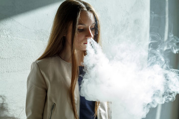 Vape teenager. Young cute girl in  casual clothes smokes an electronic cigarette near the wall...