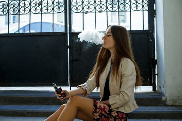 Vape teenager. Young cute girl in casual clothes smokes an electronic cigarette near the wall in...