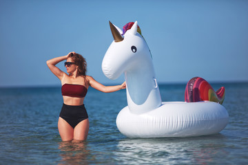 beautiful girl in bikini swimming on giant unicorn during summer vacation