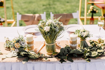 The chairs and table for guests, decorated with candle and floral arrangement, served with cutlery, crockery. Wedding banquet on a green lawn in the field, on the territory of the stable. Deer farm.