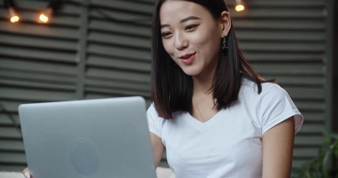 Expressive panasian woman having a video chat with friends. Pretty girl on long distance relationship. Student talking via internet and smiling - communication concept 4k