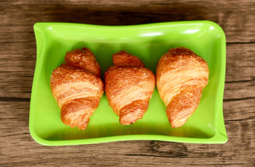 Croissants on green plate. Wood background. 
