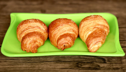 Croissants on green plate. Wood background. 