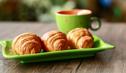 Croissants on green plate and a cup of drink. Wood background. 