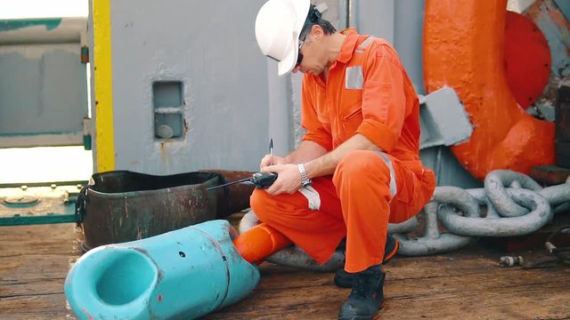 Marine chief officer or chief mate on deck of ship or vessel. He fills up ahts vessel checklist. Ship routine paperwork. He holds VHF walkie-talkie radio in hands.