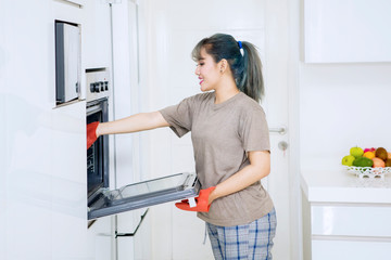 Young woman putting a baking tray into an oven