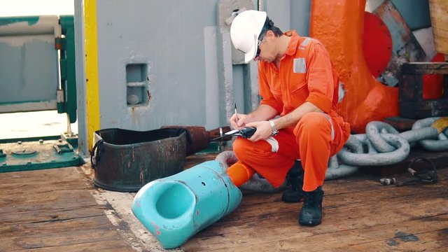 Marine chief officer or chief mate on deck of ship or vessel. He fills up ahts vessel checklist. Ship routine paperwork. He holds VHF walkie-talkie radio in hands.
