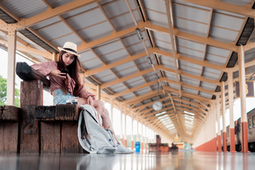 Obraz na płótnie Canvas Smiling woman traveler with backpack holding smartphone on holiday relaxation at the train station,relaxation concept, travel concept