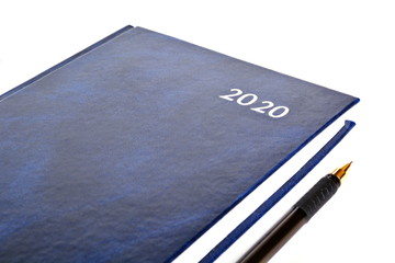 Closed blue leather notebook for new year with text 2020 on cover and office black ballpoint pen on white background. Isolated