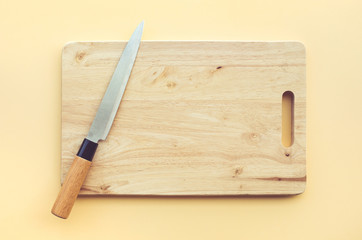 Knife on wooden chopping board on pastel color