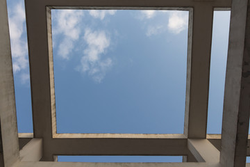 Looking up at the frame formed by concrete pillars and beams of modern buildings against a blue sky background