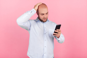 Portrait of a beautiful fox man with a beard dressed in a white shirt. With one hand he holds his head, he is shocked by what he saw on his phone. stands in front of the pink background