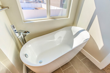 Bathroom interior with a gleaming bathtub against white wall and gray floor