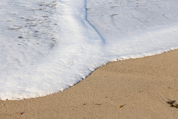 foaming breaking wave and backwash foam on a sandy shoreline