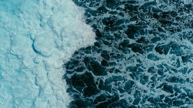 aerial drone image top looking down of surf waves rolling over a reef with white water break
