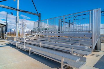 Raised tiered rows of benches with railings at a sports filed on a sunny day