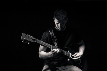 one man, playing guitar, dark and moody rock musician. Dark and moody atmosphere and lights. Shot on black background behind.