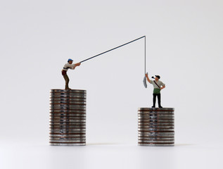 Miniature people fishing with coin piles. The concept of income inequality.
