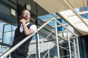 Young african american business man in suit and eyeglasses talking on the phone on the background of the business center