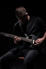 Obraz premium one unrecognizable man, playing guitar, dark and moody rock musician. Shot on black background behind.