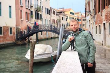 Fototapeta na wymiar Man in Venice. Portrait of handsome young man leaning against railing on walking street on narrow canal in Venice, Italy
