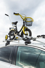 Bicycle transportation - a children's bicycle on the roof of a car against the sky in a special mount for cycling. The decision to transport large loads and travel by car