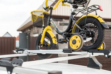 Bicycle transportation - a children's bicycle on the roof of a car against the sky in a special mount for cycling. The decision to transport large loads and travel by car