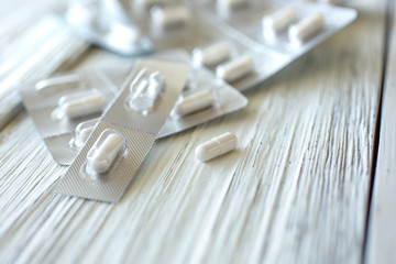 Several pill capsules still in its package, with one pill open and on a rustic white wooden table surface