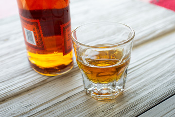 A whiskey bottle and shot glass on a rustic wooden surface