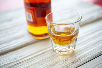 A whiskey bottle and shot glass on a rustic wooden surface