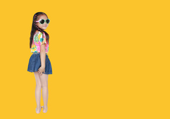 Happy little Asian kid girl wearing a flowers summer dress and sunglasses isolated on yellow background with copy space. Summer fashion kid concept.