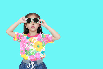 Cute little Asian kid girl wearing a flowers summer dress and sunglasses isolated on cyan background with copy space. Summer and fashion concept.
