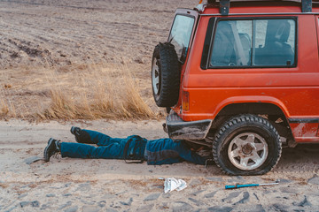 man lies under a 4x4 car on a dirt road