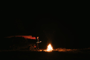 Woman sitting and getting warm near the bonfire in the night forest.