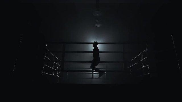 Male boxer wrapped in bandage jumping on the skipping rope in the dark ring. Slow motion. Silhouette. Boxing concept.