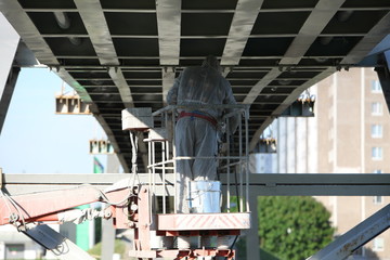 Professional worker in a protective suit and mask paints a bridge from the spray gun  stand on the hydraulic lift.