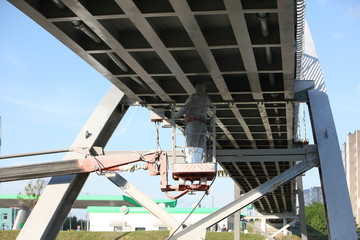 Professional worker in a protective suit and mask paints a bridge from the spray gun  stand on the hydraulic lift.