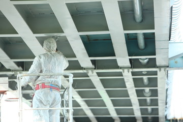Professional worker in a protective suit and mask paints a bridge from the spray gun  stand on the...
