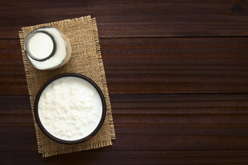 Kefirknollen in Milch in Schüssel und Milch in Flasche an der Seite, fotografiert mit natürlichem Licht