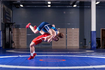 Two young men in blue and red wrestling tights are wrestlng and making a suplex wrestling on a yellow wrestling carpet in the gym. The concept of fair wrestling - obrazy, fototapety, plakaty