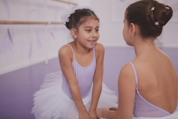Cute young ballerina enjoying talking to her friend after exercising together at ballet school. Two little girls resting after ballet class, copy space