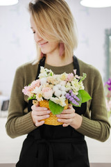 A woman florist in a black apron holds a floral composition in her hands. Young female flower seller smiling looking at bouquet.