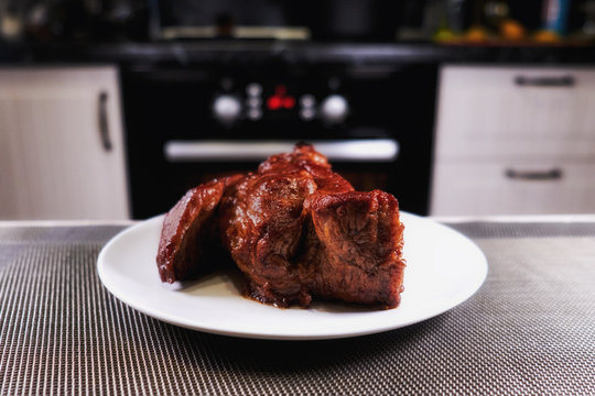 Nice piece of meat on plate. Roast beef close-up. Barbecue meat in modern kitchen. Blurred background oven. Hot cooked dinner. Delicious steak on a white plate.