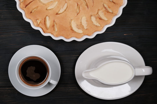 Apple Pie And Cup Of Coffee And Creamer. Homemade Cakes Of Ripe Apples On A Black Wooden Background. Fruit Cake In A Baking Dish.