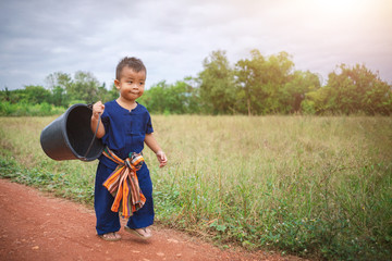 Child walking carrying a bucket.