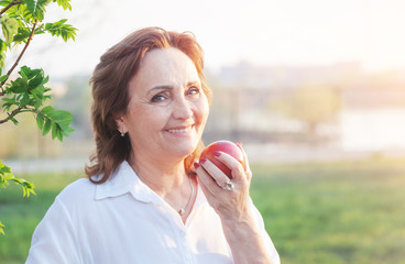 Beautiful happy smiling elderly woman holding a red apple in her hands, healthy diet concept