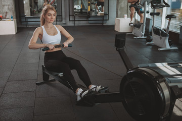 Top view of a beautiful young fitness woman working out on rowing machine. Attractive athletic woman doing cardio workout, using row machine, copy space